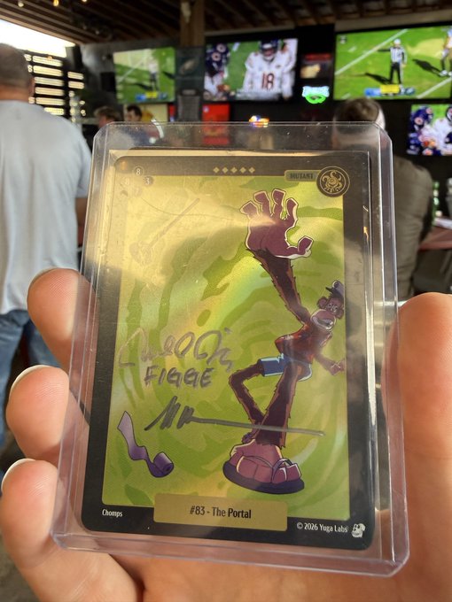 A hand holding a graded Chase & Status 'The Portal' trading card #83 in a protective case, with a sports bar showing football on TVs in the background.