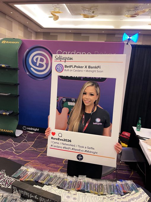 A woman holding a large Instagram-style selfie frame at a BetFi.Poker X BankFi booth at RareEvo2026, with a green backpack and promotional merchandise displayed on the table.