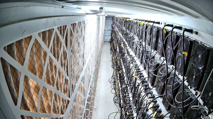 A fisheye view of a large industrial cryptocurrency mining facility with rows of mining rigs and cooling fans.