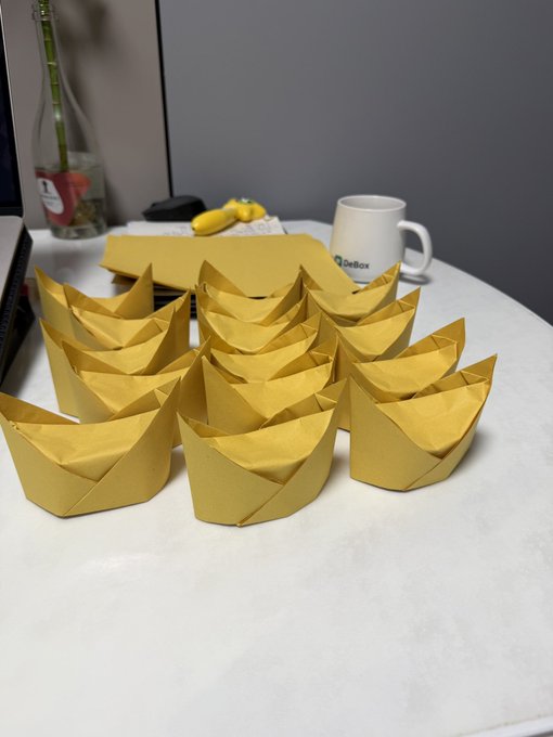 A collection of yellow paper fortune cookies sits on a table, fitting with the caption's theme about believing in fate and being a fortune teller. Visible text includes "DeBox" on a white mug and "B" on a glass bottle in the background.