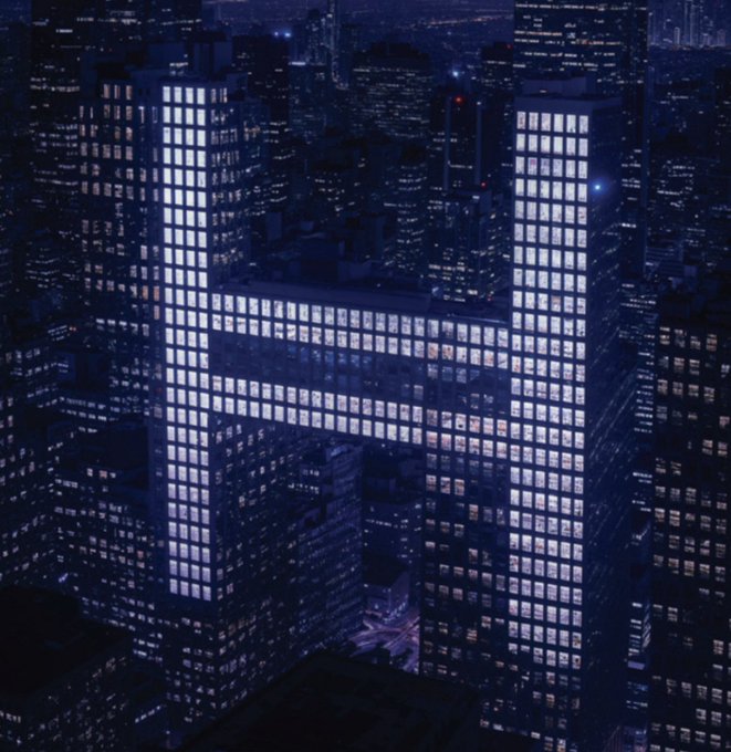 A nighttime aerial view showcases a distinctive H-shaped skyscraper with illuminated windows standing prominently among surrounding city buildings. The bold architectural silhouette and glowing "H" formation visually reinforce the caption's clever wordplay on "DLT"—suggesting that standing out with a unique shape (and initial) is the chic choice.