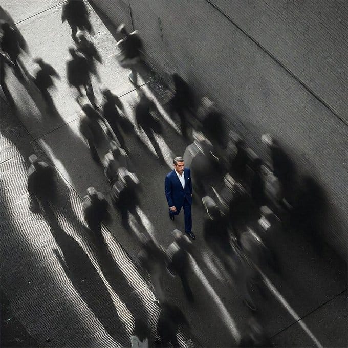 The image shows a man wearing a suit walking down a street, surrounded by many other people who are also dressed up for an event or occasion. The scene appears to be captured from above, giving a bird's eye view of the crowd below. The focus on the man in the suit and his surroundings highlights the importance of the event or gathering taking place. This image could potentially be related to the post about Ethereum, as it emphasizes the idea that while everyone is busy hunting for the next 100x return, there are still assets like tokens that can outperform over time.