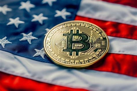 A close-up photograph of a gold-colored physical Bitcoin token resting on an American flag.