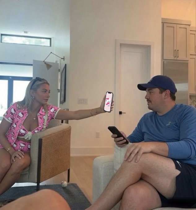 A woman in a pink Hello Kitty outfit shows her phone screen to a man wearing a navy cap and blue shirt, with the displayed image appearing to feature a cat, playfully tying into the post's bullish take on $KITTY as the memecoin of the cycle.
