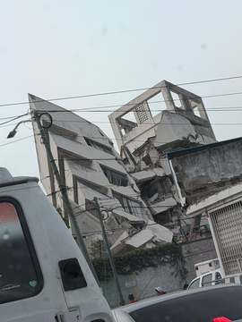 A multi-story building stands collapsed and crumbling in the aftermath of destruction, illustrating the urgent humanitarian crisis in Venezuela that the post is seeking donations to address. A white truck is parked in the foreground, with no visible text or wallet addresses in the image.