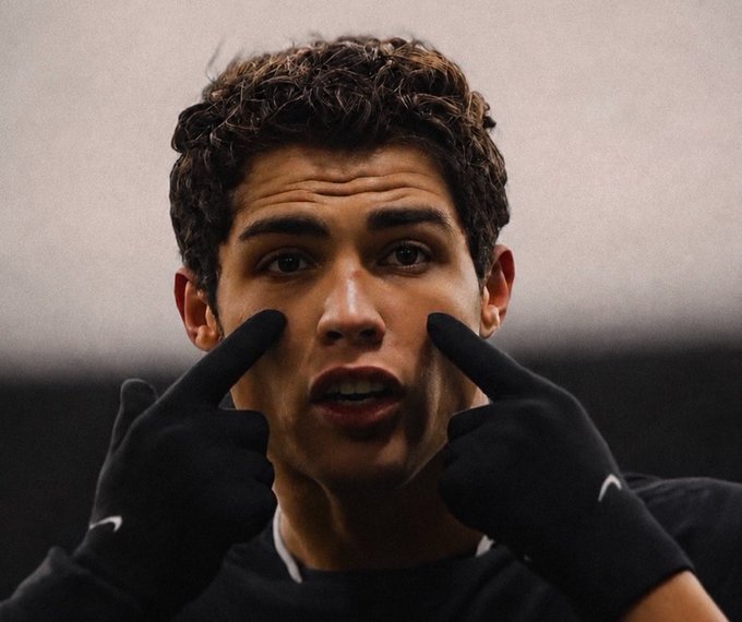 A young man with curly brown hair wearing black Nike gloves points both index fingers at his cheeks, appearing to be a soccer player in a pre-match or training setting. The image appears unrelated to the accompanying post about a Solana cryptocurrency giveaway.