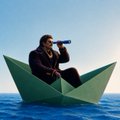 An artistic image of a person in a suit sitting in a green paper boat on the ocean while speaking into a megaphone.