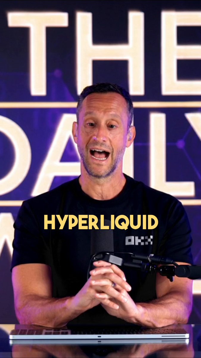 The image features a man wearing a black shirt with "HYPERLiquid" written across his chest, who appears to be giving a speech or presentation. He is standing behind a desk that has a laptop open in front of him. The background of the image includes a purple banner and a yellow logo for "THE DAILY WOZONE".