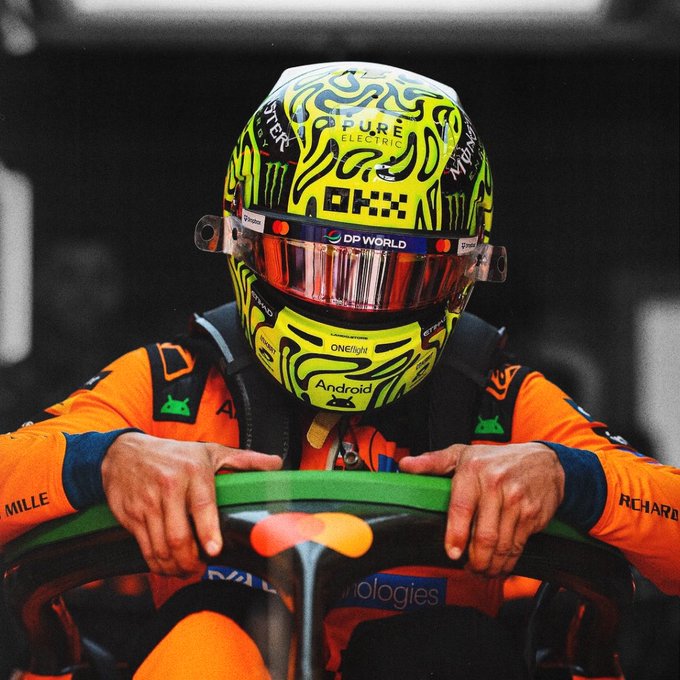 A McLaren F1 driver grips the steering wheel in their cockpit, wearing a vibrant neon yellow helmet featuring sponsors like "DP World," "Android," "Monster," and "OneLight," paired with the team's iconic orange race suit. The image captures the intense focus following a P3 qualifying result at the Belgian Grand Prix, ready to go full send in tomorrow's race.