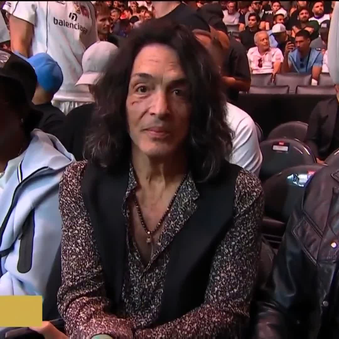 A woman with dark hair wearing a patterned shirt and black vest sits courtside at a UFC event, with the "balenciaga" logo visible on a spectator's shirt in the background, relating to the post's mention of celebrities attending UFC 331 at Crypto.com Arena, broadcast on PPlusDeportes.