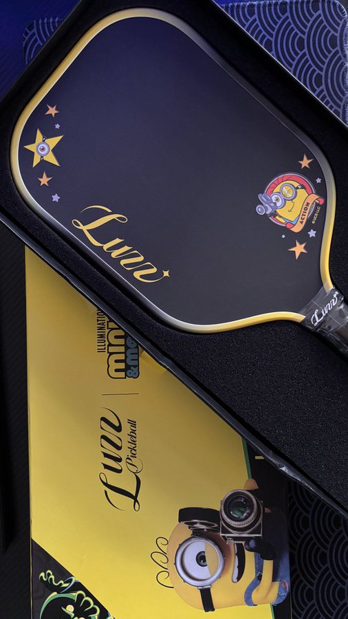 A Luxeed (Leqi Pickleball) brand pickleball paddle with a Minions collaboration design, featuring a dark blue surface with stars, a Minion character, and matching packaging.