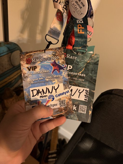 A hand holds up two VIP All Access Pass lanyards for RareEvo 2024 (August 6-10, 2025 at Caesars Palace, Las Vegas) featuring "Danny Rbar" alongside logos for Rare Evo, Prism, Ledger, and Catalyst, ready for the Cardano representative to network at the event.