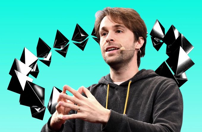 A man in a dark hoodie speaks while gesturing with his hands, with Ethereum logo diamond shapes floating in the background against a teal backdrop.