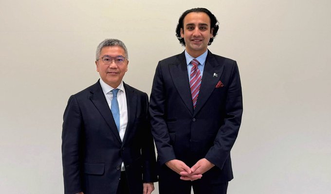 Two formally dressed men—one in a dark suit with a blue tie and another taller man in a navy suit with a red striped tie and pocket square—pose together against a plain light-colored wall, likely representing the diplomatic or business meeting referenced in the post about Pakistan and Hong Kong exploring tokenized finance and blockchain-based government bonds.