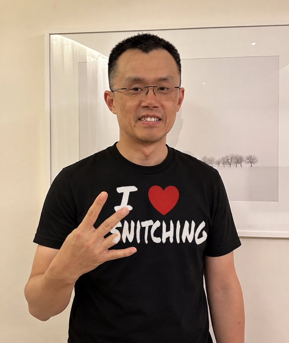 The image shows CZ (Changpeng Zhao, former Binance CEO) smiling and making a peace sign while wearing a black t-shirt that reads "I ❤️ SNITCHING"—a play on the word to hint at his commentary about Solana's Shanghai event being suspended shortly after he publicly praised their ability to operate in China.