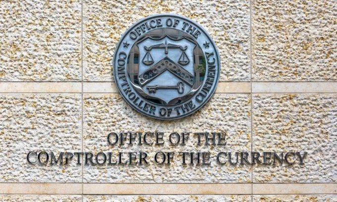 The seal and signage for the Office of the Comptroller of the Currency (OCC) are mounted on a stone building facade. The image relates to the post by visually representing the agency tasked with finalizing stablecoin regulations under the GENIUS Act.