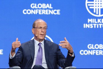 Larry Fink, CEO of BlackRock, speaks at the Milken Institute Global Conference, gesturing with both hands while seated on stage. The image provides visual context for commentary on Bitcoin's price near $65,000, though the specific message in the accompanying post warns against jumping into BTC at its current high level.