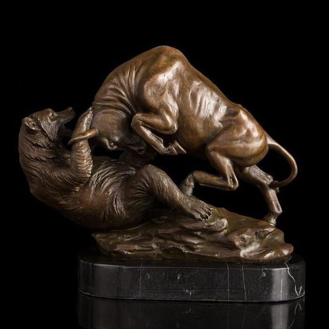A bronze sculpture depicting a dramatic scene of a buffalo attacking a bear, mounted on a dark stone base.