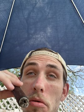 A man wearing a tan baseball cap holds a cigar near his mouth under a blue umbrella, appearing to take a break by a pool. The image captures a relaxed, poolside moment that complements the post's casual tone about gambling on StakeUsa, where a small $3 bet reportedly turned into a substantial $7,100 win.