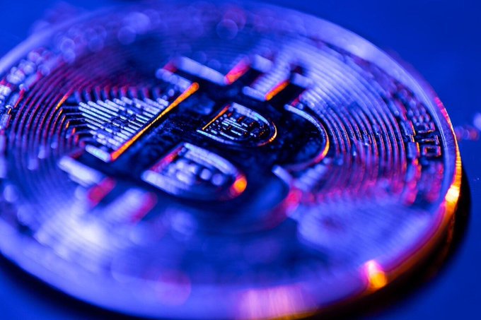 A cryptocurrency coin with a Bitcoin "₿" symbol glows with blue and orange light against a dark background, visually representing the digital currency at the heart of the article about Brazilian contributions to Bitcoin's global development.