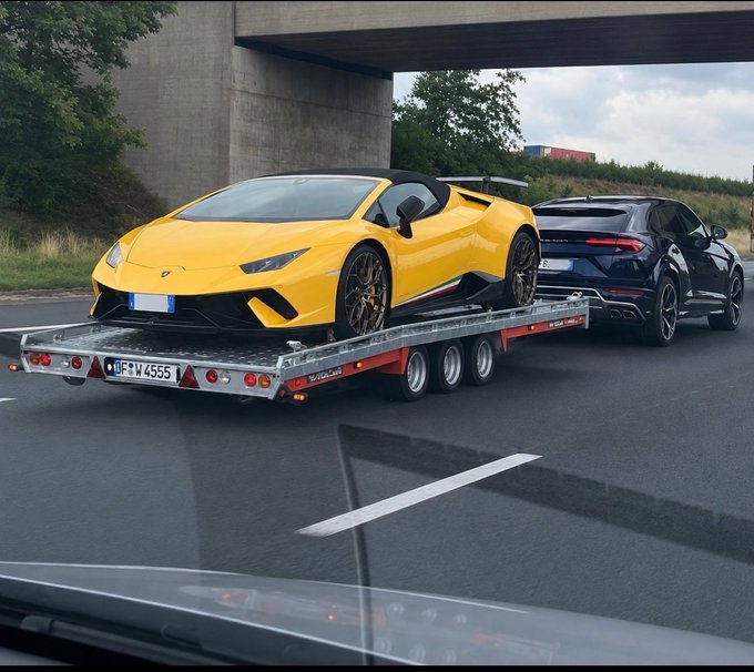 A yellow Lamborghini Huracán Performante Spyder is loaded onto a flatbed trailer with the license plate "OF W 4555," being towed by a black Lamborghini Urus on a highway. The image conveys a sense of high-end luxury and motion, aligning with the post's theme of anticipating wealth and the thrill of moving up once the market picks up.