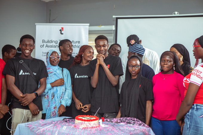 A group of smiling young people gather around a cake at an event for 'Building The Future of Avastars in Africa,' with several wearing shirts branded 'Avastars.'