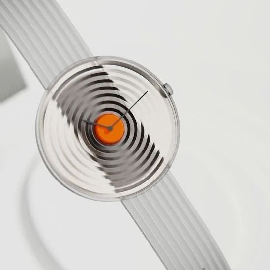 A close-up of a modern wristwatch with a silver ribbed band and a face featuring black and white concentric circles with an orange center.