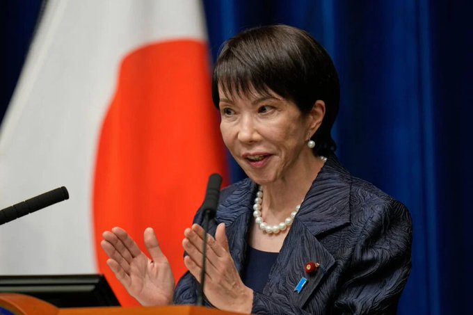 A woman in a pearl necklace gestures while speaking at a podium in front of the Japanese flag, as the country prepares to allow USDC for international settlements.
