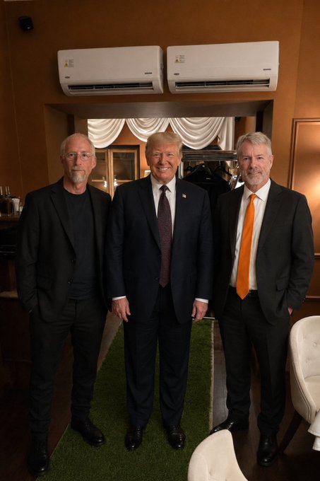 The image shows three men standing together, posing for a photo. They are all dressed formally, with one man wearing a suit and tie, another wearing an orange tie, and the third wearing a black suit. The room they are in appears to be a restaurant or dining area, as there is a chair visible in the background. The post about BitcoinPrague suggests that this gathering might have taken place at a location where Bitcoin transactions occur, possibly involving international business or financial matters.

The three men seem to be enjoying their time together and are smiling for the photo. They are standing close to each other, with one man on the left side of the image, another in the center, and the third on the right side. The room has a brown color scheme, which complements the formal attire of the men.