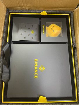 A Binance promotional box containing a black notebook with the yellow Binance logo and a small yellow Binance plush toy.