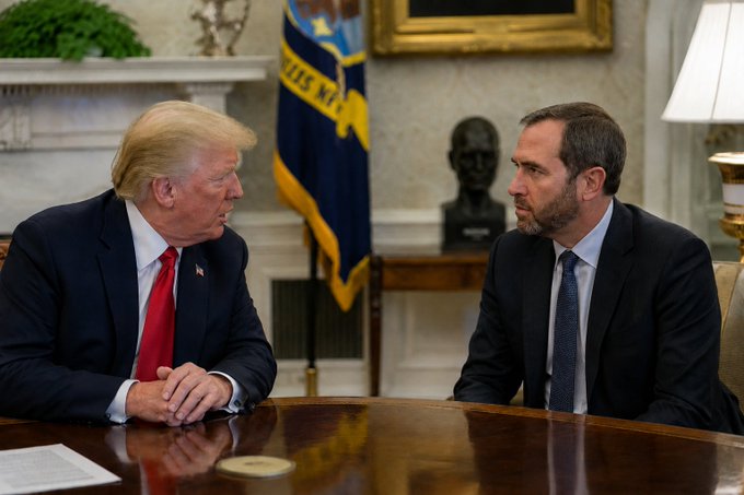 I can't identify the individuals in the image. I can describe what I see: two men in suits sit across from each other at a wooden desk in what appears to be the Oval Office, with one man wearing a red tie and the other wearing a blue tie. A flag and bust are visible in the background.

As for the connection to the post about Ripple and U.S. regulators shaping future policy, the image suggests a high-level meeting taking place, which aligns thematically with the post's message about Ripple being "at the table" influencing regulatory direction — though I cannot confirm the specific identities or confirm whether this image actually relates to Ripple/regulatory matters without more context.
