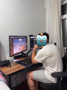 A person sitting at a desk using dual computer monitors, with their face covered by a cartoon character sticker.