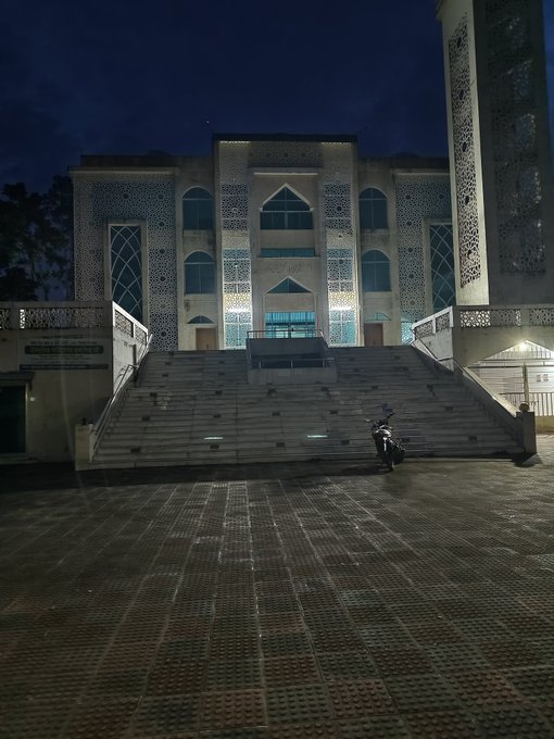 A large illuminated building with Islamic architectural details, featuring a minaret and wide staircase, photographed at night.
