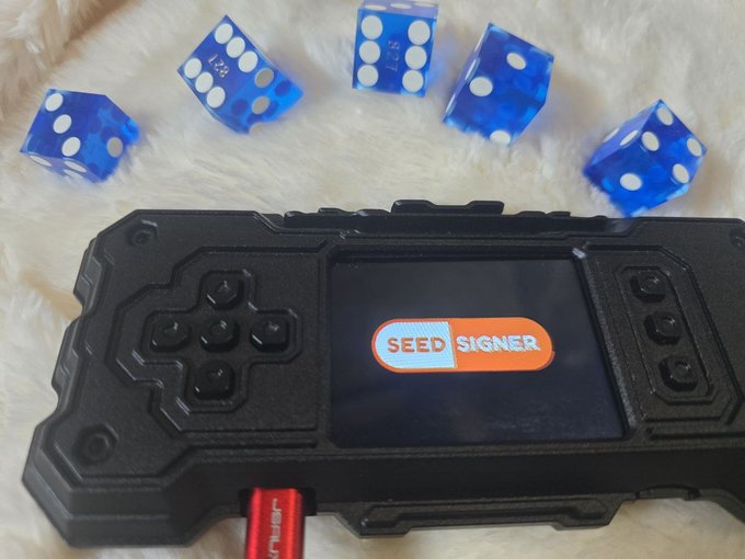 A black crypto hardware wallet displaying 'SEED SIGNER' on its screen, resting on a white furry surface alongside five translucent blue dice.