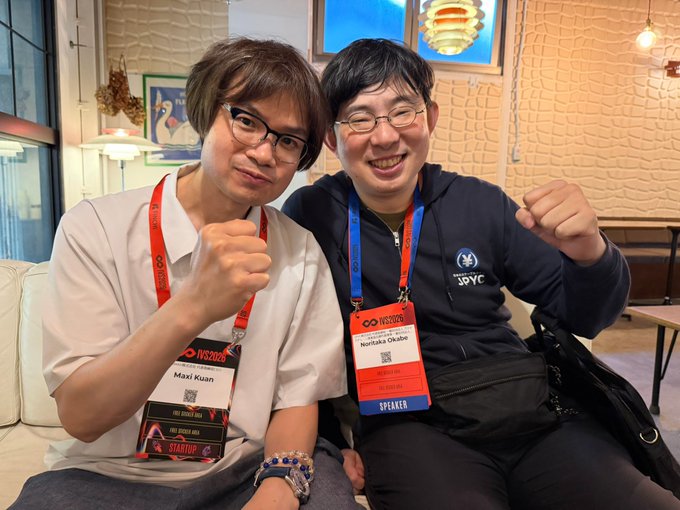 Two men pose enthusiastically with raised fists at IVS Kyoto, wearing speaker lanyards identifying them as "Maxi Kuan" (STARTUP) and "Nontaka Okabe" (SPEAKER), celebrating the JPYC stablecoin and The New Elemental Knights' JPYC compatibility.