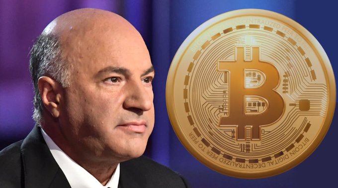 A man in a suit stands beside a large golden Bitcoin (BTC) coin against a blue background.