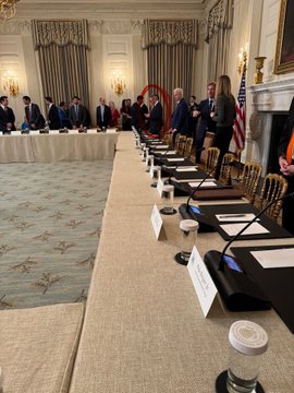 A formal meeting room setup with long tables, microphones, and name placards arranged in an elegant White House parlor, alongside an American flag. The image supports the post about Ripple executives attending a White House meeting related to $XRP, showing the official venue where such high-level discussions would take place.