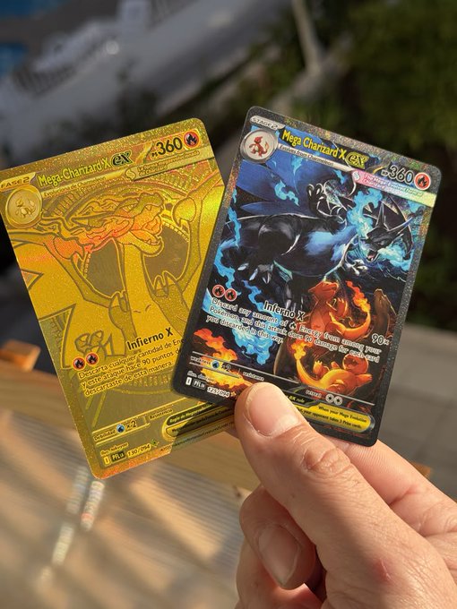 A hand holding two Pokémon trading cards, including a gold Mega Charizard ex and a black-bordered Mega Charizard X ex, against a bright outdoor background.