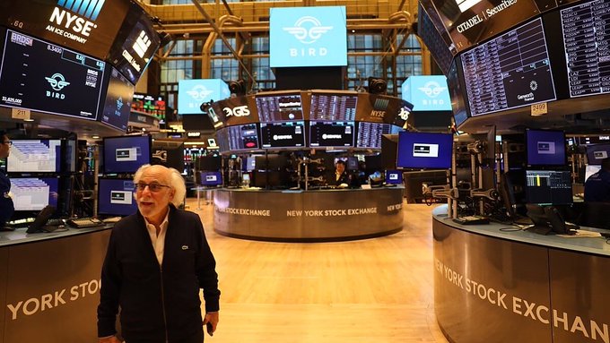 A man with white hair standing on the floor of the New York Stock Exchange, with 'NYSE' and 'BIRD' (Bird scooter logo) displays visible in the iconic trading floor.
