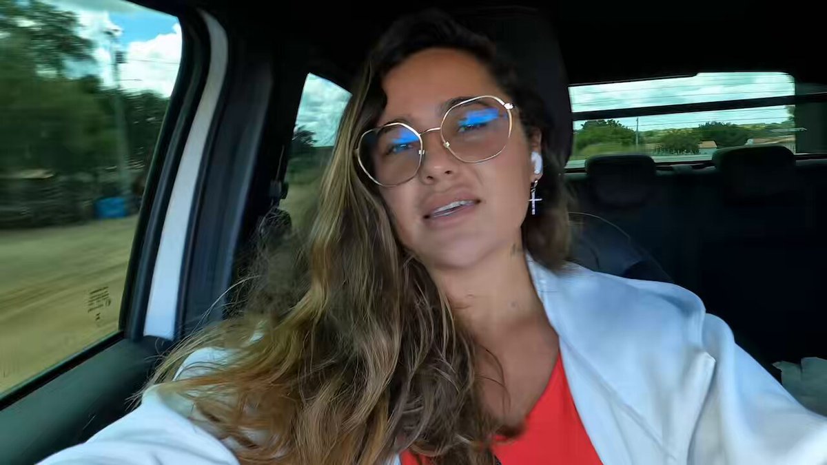 The image shows a woman wearing glasses sitting inside a car with her head tilted back as she looks out of the window, possibly enjoying the view or daydreaming. The photo has been edited to include text that reads "RoadTrip RN ➜ Maranhão pagando com cripto! Enquanto viajo, meu dinheiro trabalha por mim, com apenas R$500 em gastos, recebi R$100 de cashback pelo Odyssey Program da Bitget Wallet. @BitgetWalletPT". The woman's position in the car and her tilted head back are central to the image, while the edited text is placed around her, creating a sense of depth and context for the scene captured in the photo.