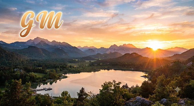 A sunrise landscape over mountains and a lake with the cursive text 'gm' (good morning) overlaid in golden letters.