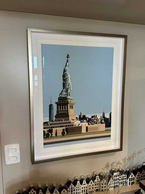 A framed print of the Statue of Liberty hangs on a beige wall, with a small decorative village display visible below it.
