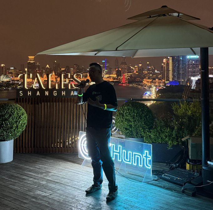 A man singing into a microphone on a rooftop at night, standing next to a neon 'Hunt' sign, with the illuminated Shanghai skyline visible in the background.