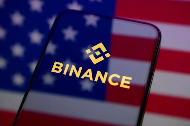 The image features a smartphone holding up an American flag with a "Binance" logo positioned above it. The phone's screen displays the text "Binance launches U.S. stock trading service for users outside the United States, with fractional shares available starting at just $5". This suggests that the Binance platform is now accessible to people outside of the United States, providing them with a way to purchase and invest in US stocks through the platform.