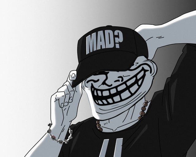 A black-and-white troll face meme wearing a cap that reads "MAD?" tips its hat while grinning widely, perfectly capturing the cheeky "trolling" spirit referenced by the $TROLL memecoin mentioned in the post. The image visually embodies the irreverent, meme-driven branding that memecoin projects like $TROLL leverage to build IP and community.