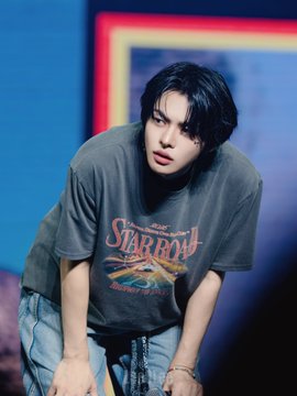 A young man with dark hair wearing a gray "Star Row" graphic t-shirt and light jeans is leaning forward, with hashtags referencing LEO and ALPHADRIVEONE (ALD1) suggesting this is a photo of the K-pop artist LEO from the group ALPHA DRIVE ONE.