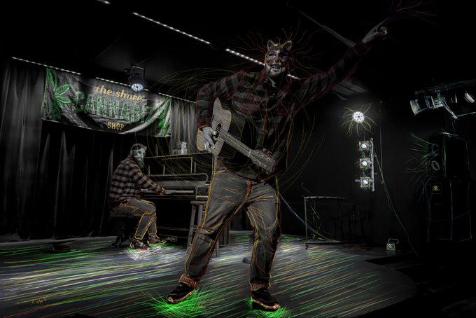 A stylized digital artwork of a musician playing a guitar on stage with neon light trails, with a banner reading 'The Shore Mallards Shop' in the background.