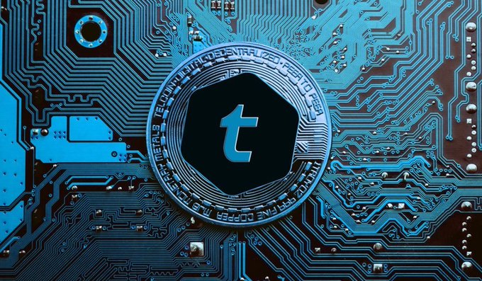 A blue-tinted graphic image of a circuit board with a central black hexagonal token displaying a stylized 't' logo, resembling cryptocurrency branding.