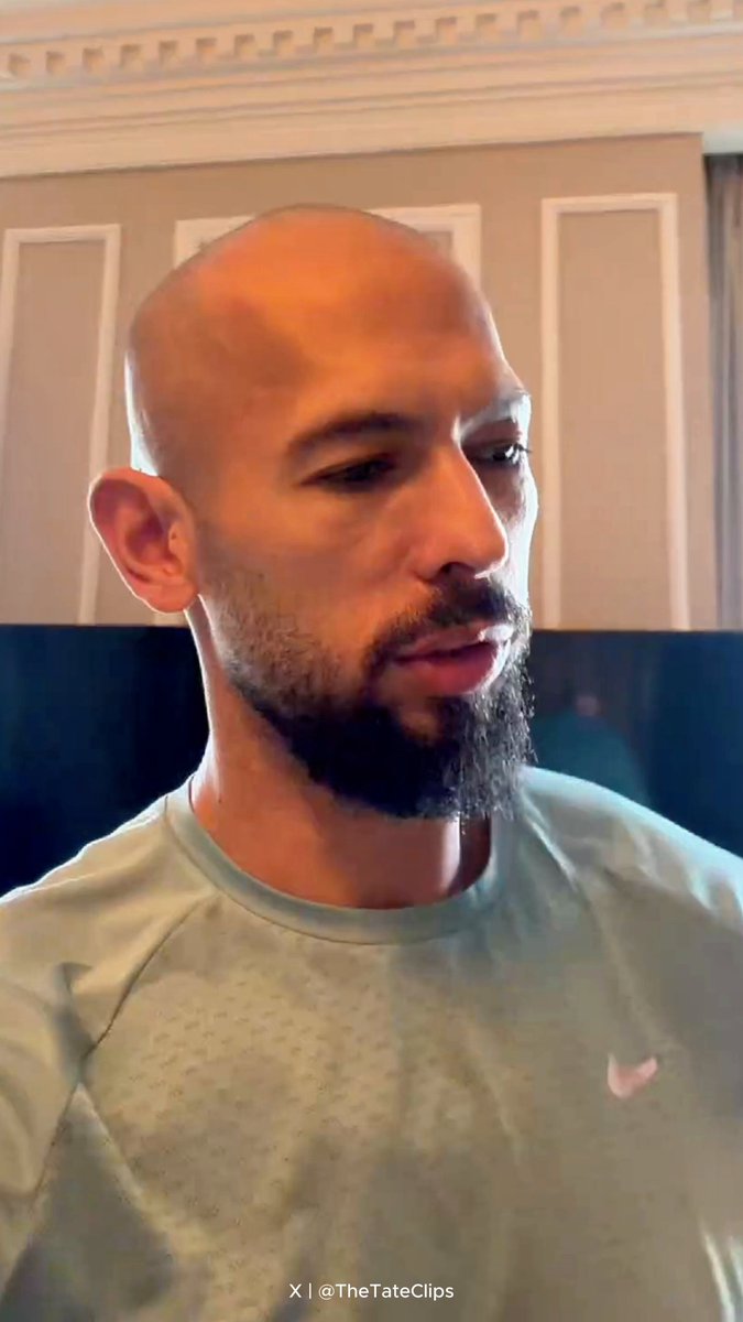 The image shows a bald man with a beard wearing a gray shirt standing in front of a television screen or monitor displaying information related to Bitcoin prices. The caption suggests that Andrew Tate is investing in Bitcoin, which has increased in value by over $26,000 since 2015. This implies that Andrew Tate's investment has performed well and he might be considering other Bitcoins as well or potentially expanding his cryptocurrency collection.