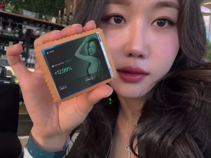 A young woman holding a small digital display showing a stock chart with '+12.99%' and 'Meta token (META)', alongside a photo of herself.